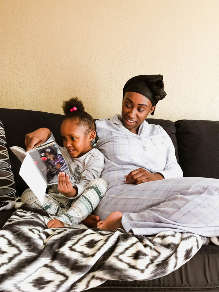 A mother and her daughter smile while looking at a photo album while sitting on a couch.