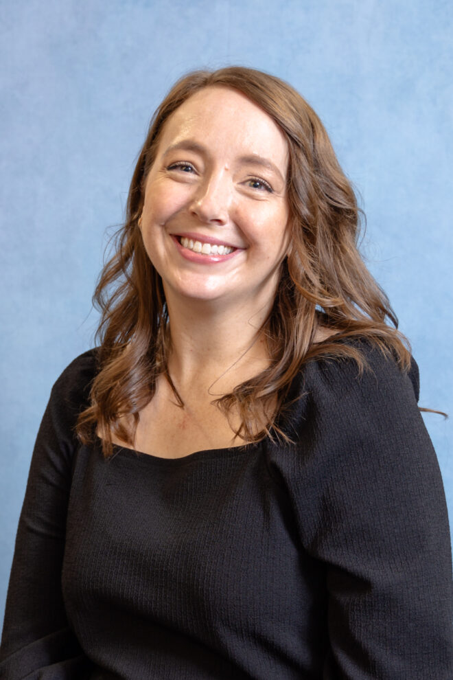 Andrea Vanni smiles at the camera in front of a blue background