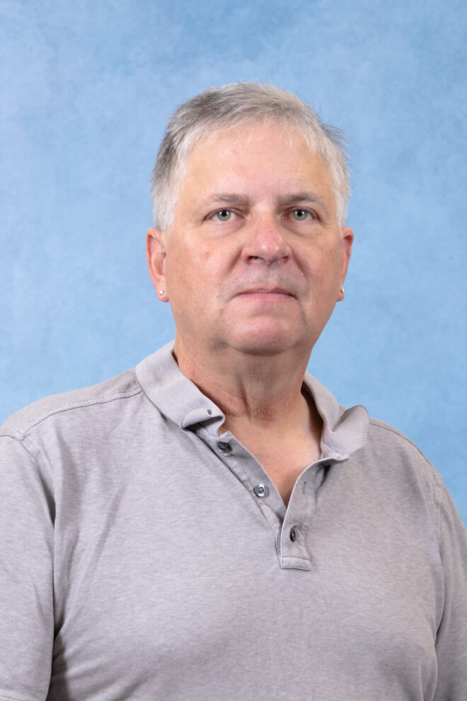 Jim Collier looks at the camera with a serious expression in front of a blue background