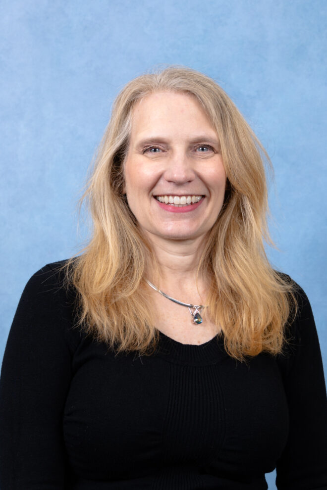 Noelle Nicholas smiles at the camera in front of a blue background