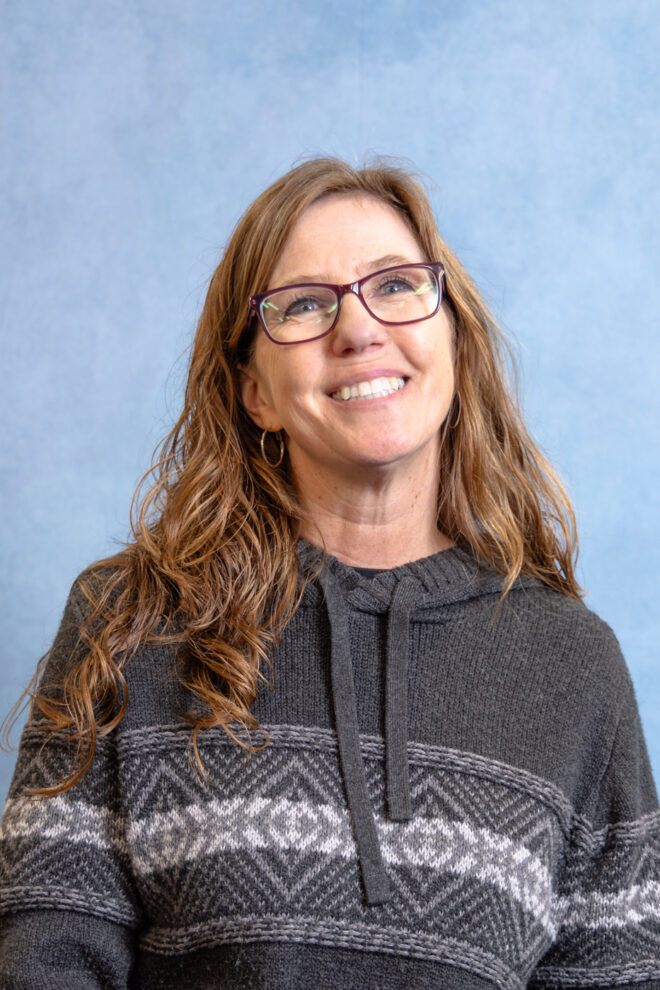 Tracy Hubbell smiles at the camera in front of a blue background